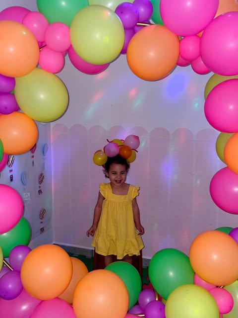 Menina de vestido amarelo sorrindo em um arco de balões coloridos