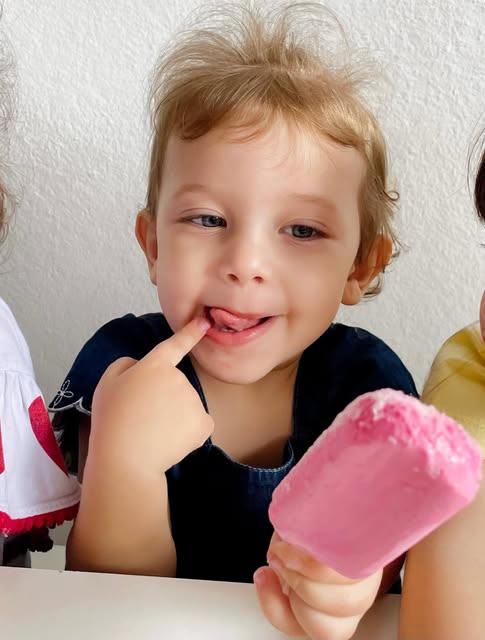 Menino lambendo os dedos com um picolé rosa